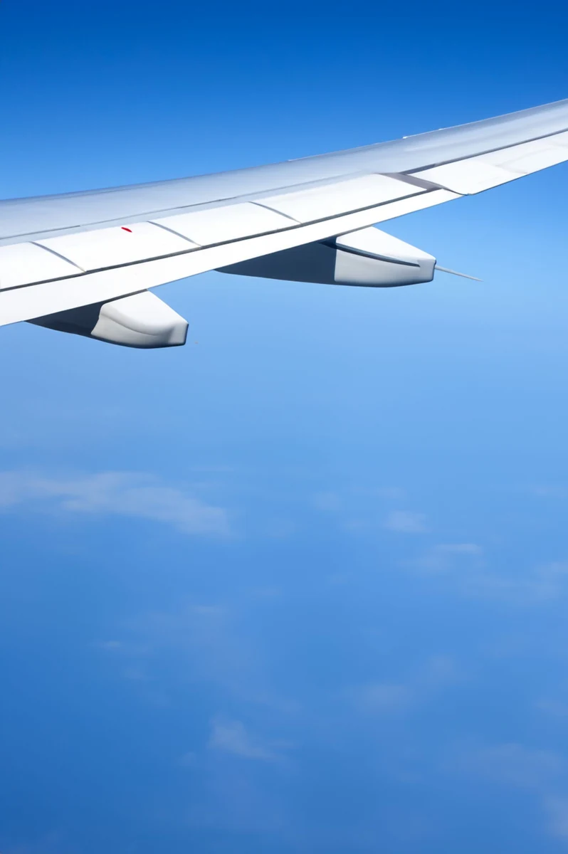 Asa branca de um avião vista durante o voo, sobre céu azul.